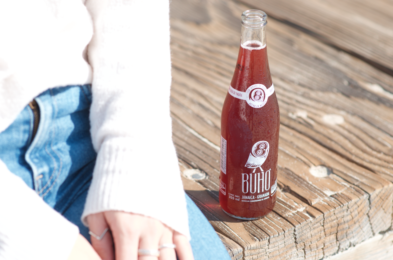 A Bottle of Buho Soda on a Wooden Deck standing next to a sitting woman