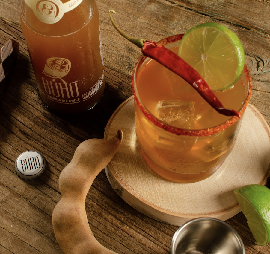 A bottle of Buho Soda next to a cup of soda with a chilly laying across